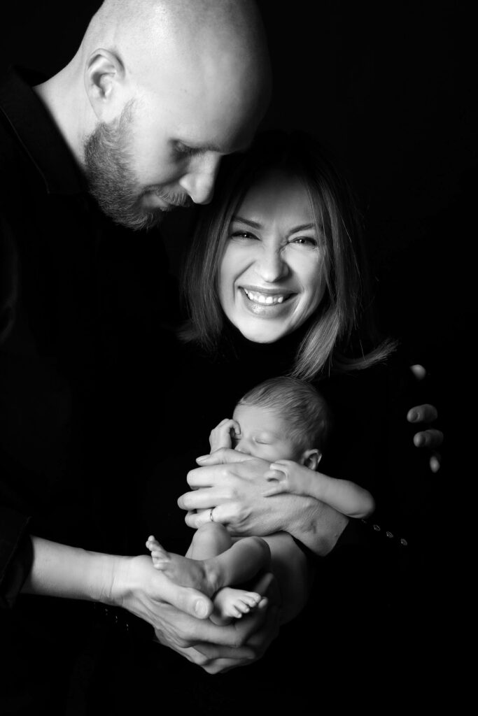 Rodina s miminkem se smějí, černobílá fotografie plná radosti ve fotoateliéru Jana Hozová v Praze.