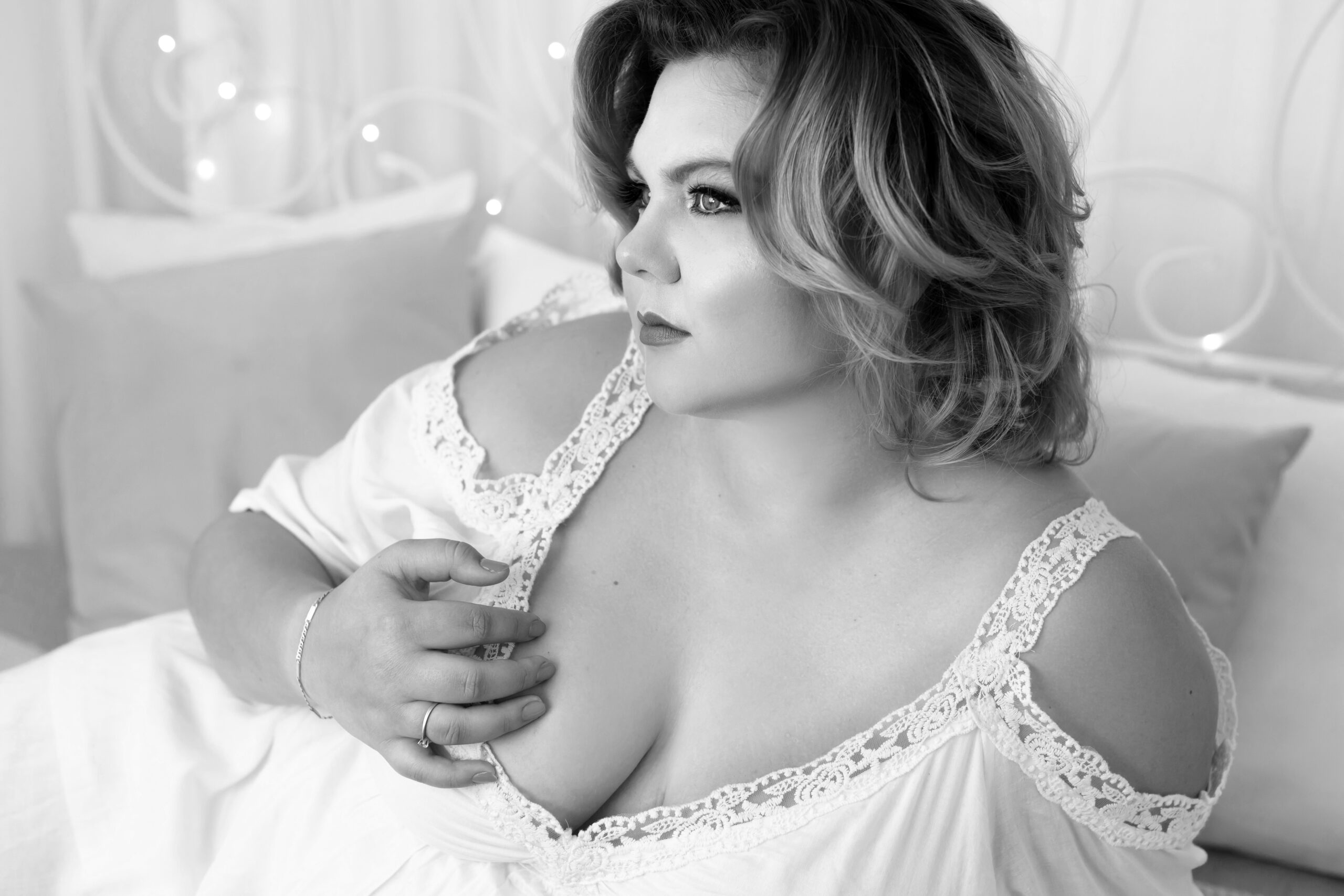 Žena na glamour focení, která je plus size modelkou a cítí se sexy v prádle na posteli.