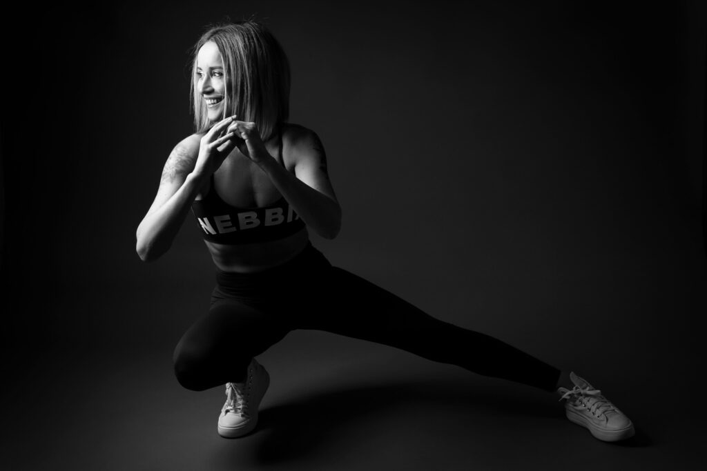 Černobílá fotografie ženy ve sportovním oblečení při bočním výpadu v ateliéru.