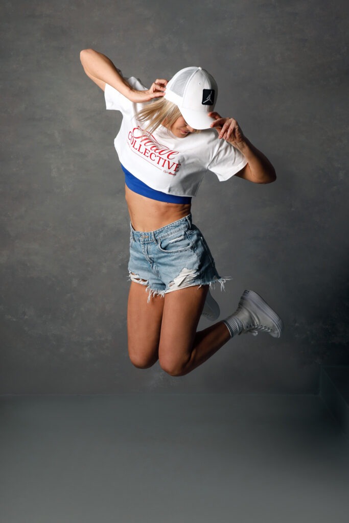 Dynamická brandová fotografie ženy ve sportovně ležérním outfitu při výskoku v ateliéru.
