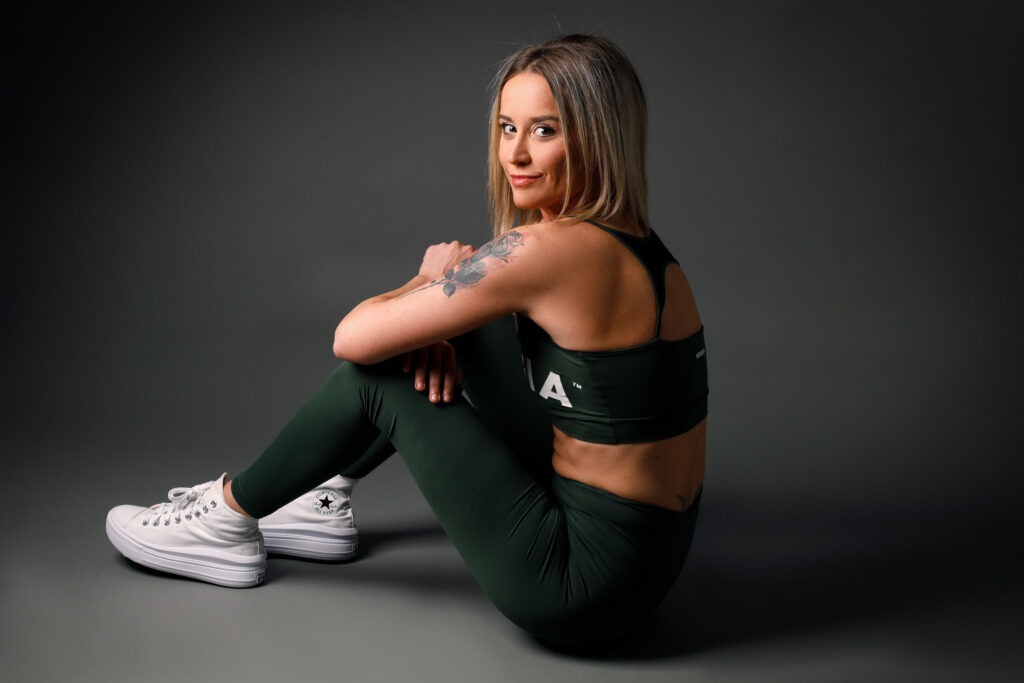 Sportovní brandový portrét ženy v zeleném fitness outfitu sedící na zemi v ateliéru.