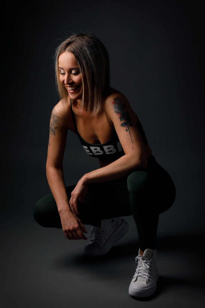 Přirozená fotografie ženy v zeleném sportovním oblečení při uvolněném pózování v ateliéru.